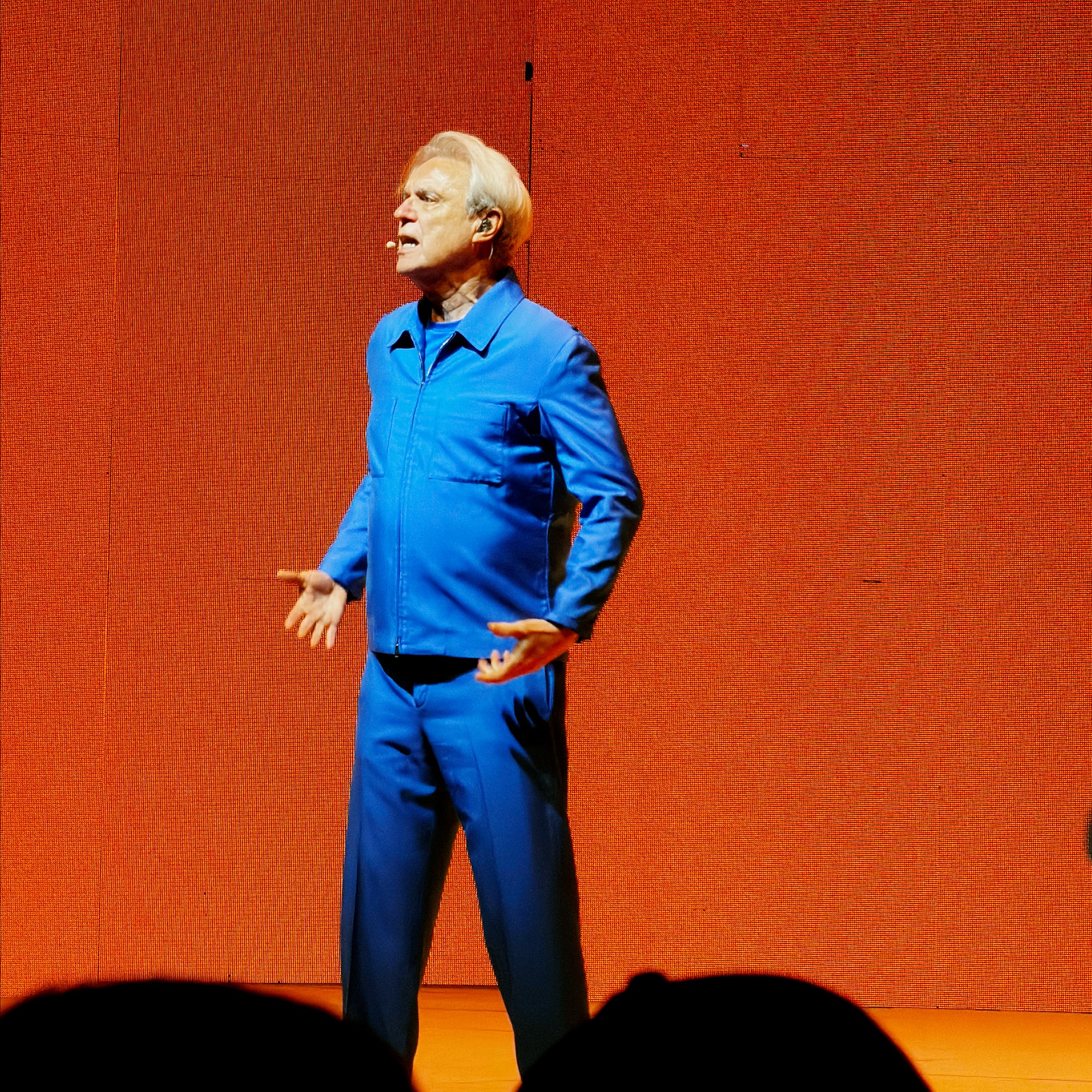 David Byrne in a bright blue suit, singing on stage in front of an orange backdrop at Starlight Theatre