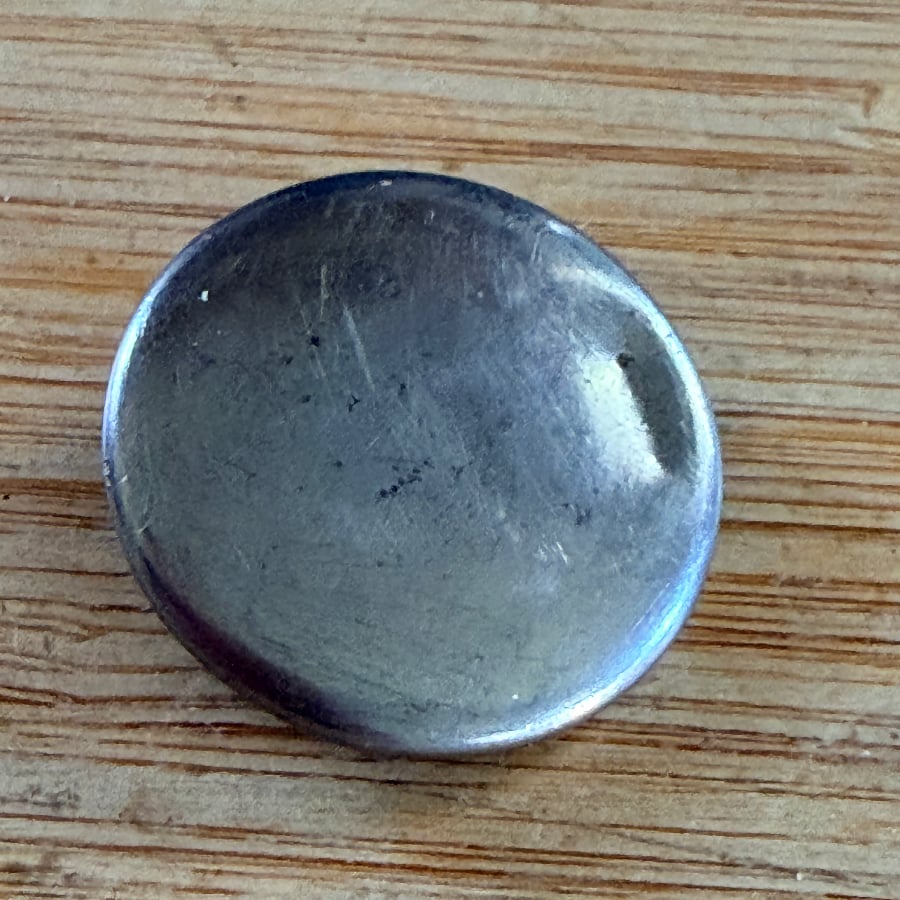 The same button with the paint scraped off, leaving a scratched silver surface, on a wooden table